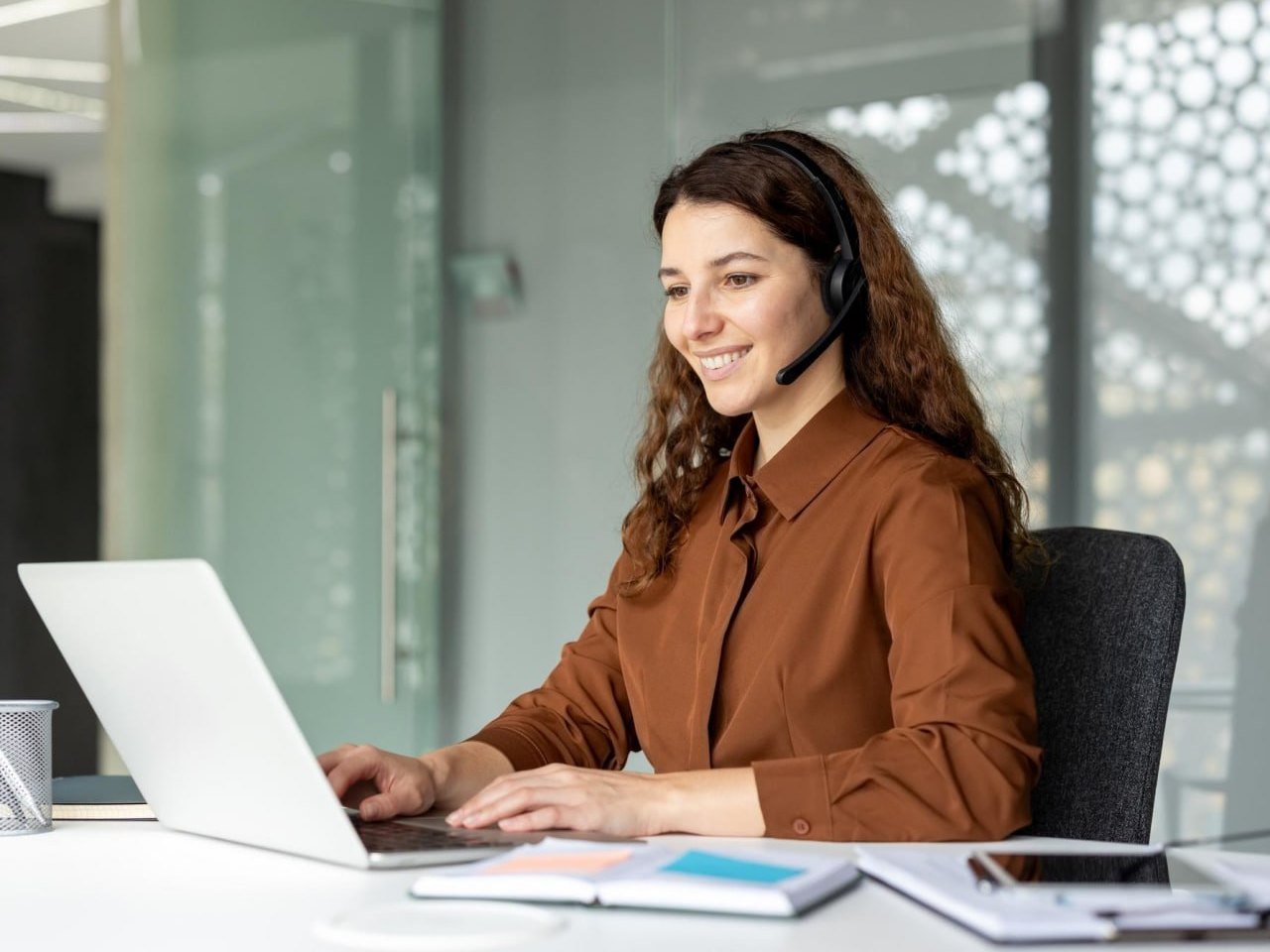 A virtual assistant on a headset, smiling at her laptop in a bright office